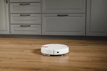 Robot vacuum on a hardwood floor in a kitchen, drawers in the background.